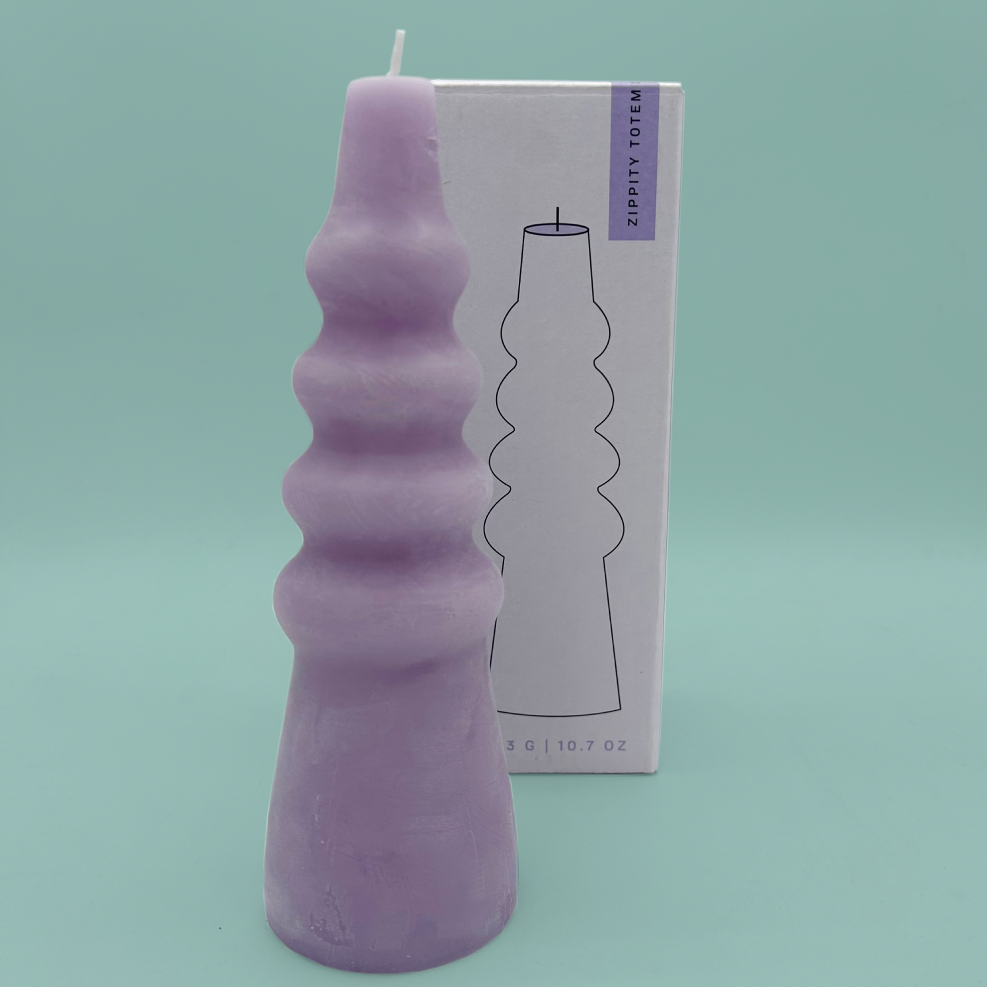 A lilac candle in a wiggly pillar shape, in front of a purple box.