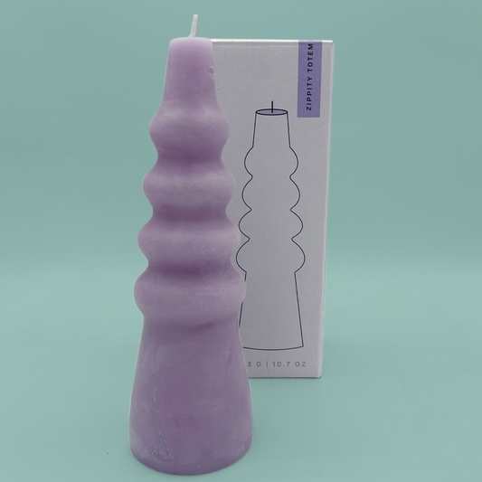 A lilac candle in a wiggly pillar shape, in front of a purple box.
